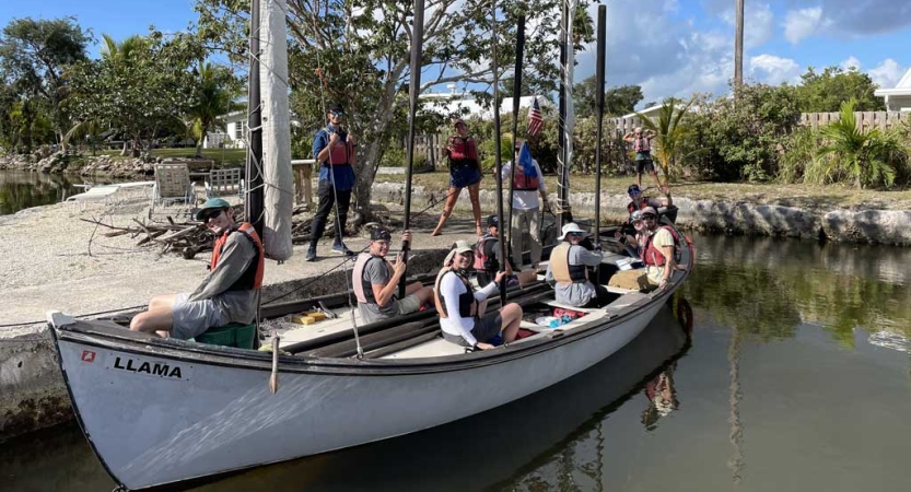 A group of people sit together on a docked sailboat and smile for the photo